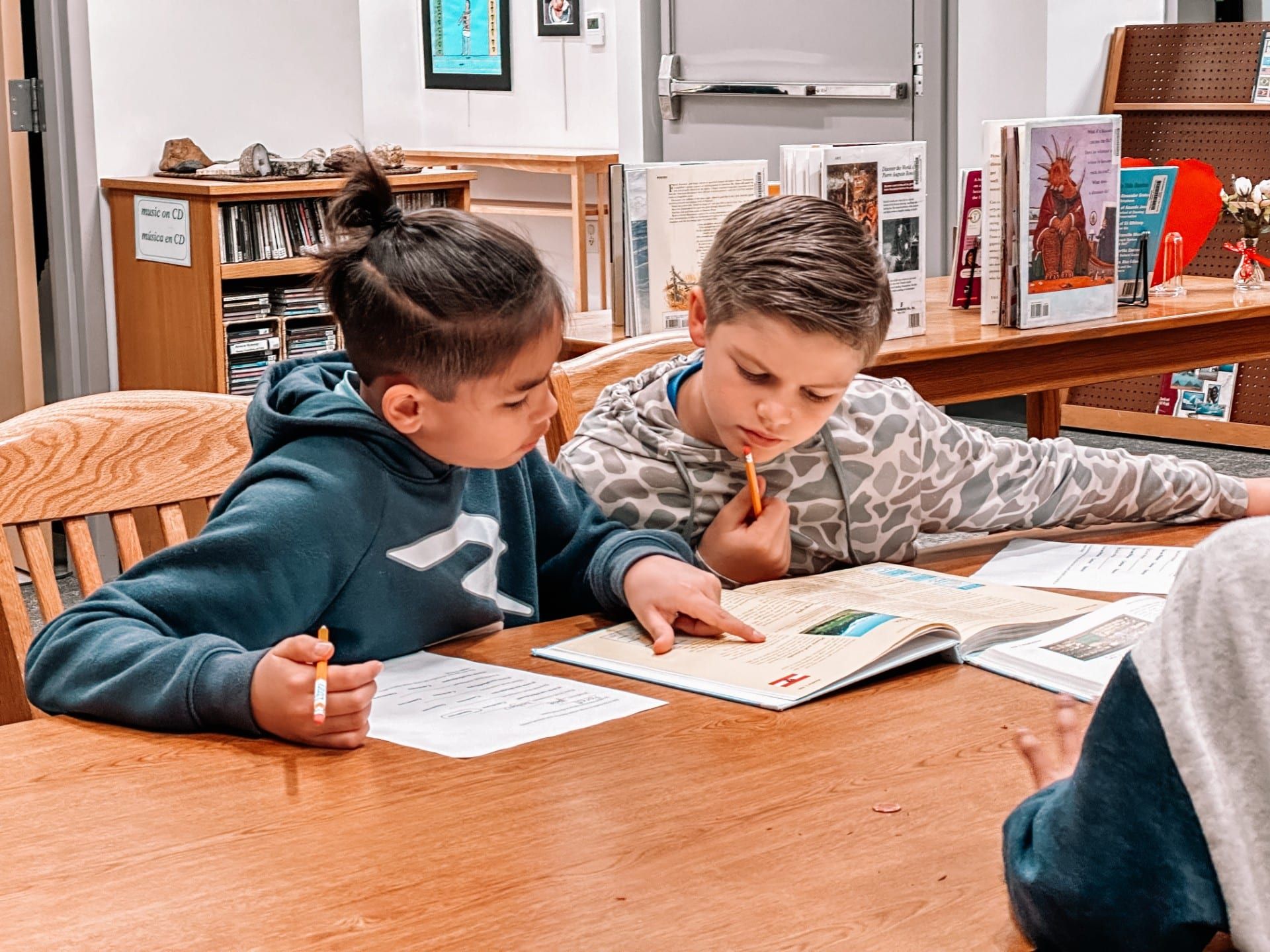 Two children studying a book together at a wooden table in a library.