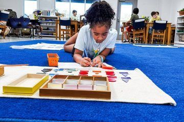 Girl on floor working with Montessori materials. Classroom setting with blue carpet.