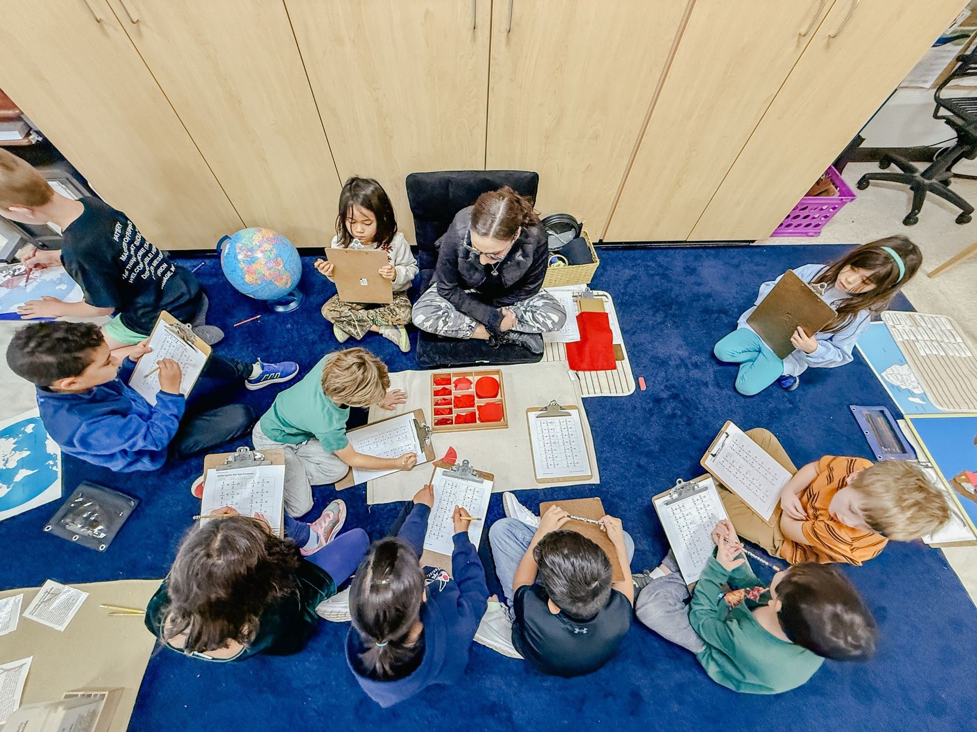 Small group surrounds teacher and uses clipboards and fraction tiles to add fractions with common denominator.