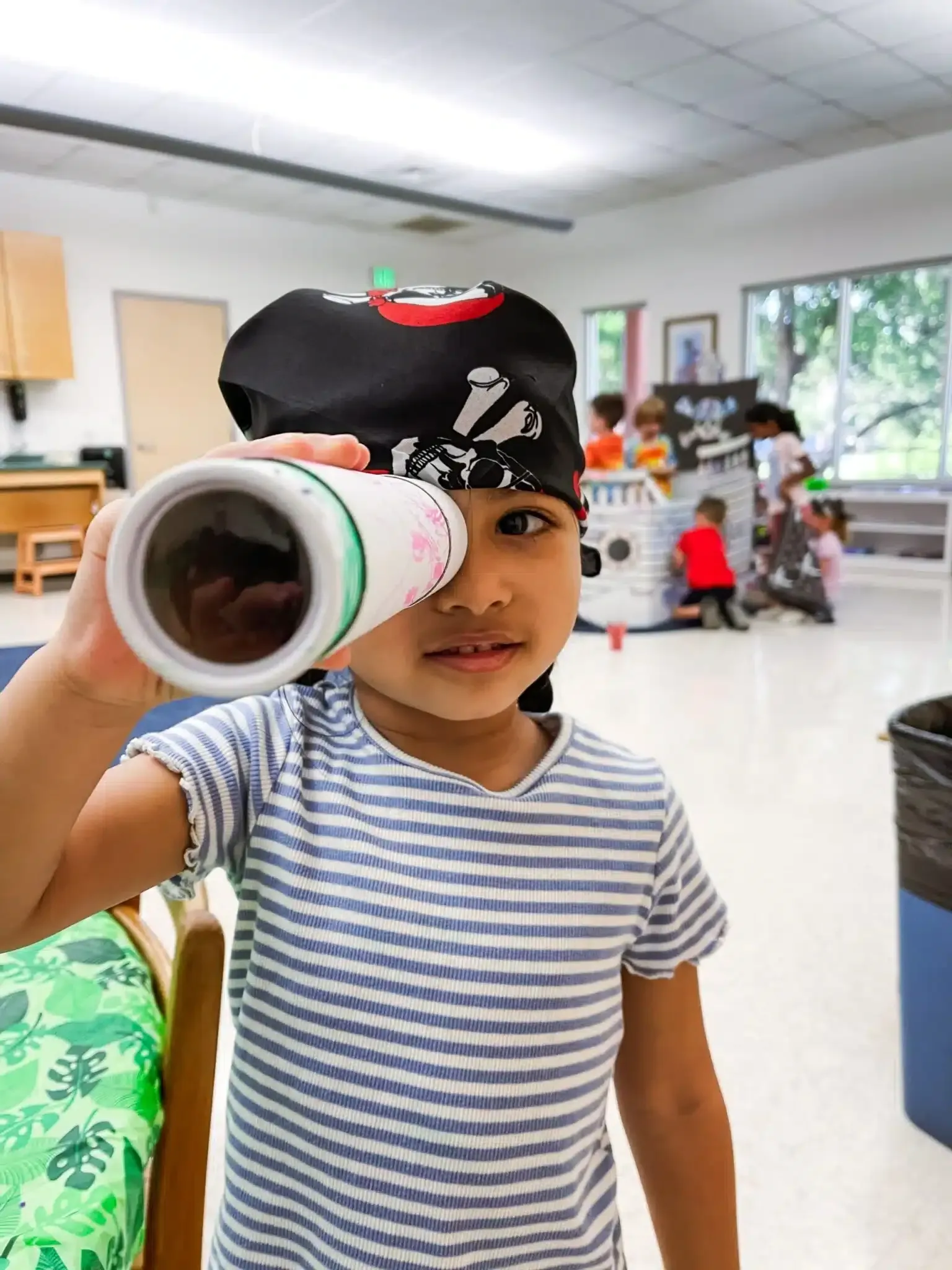 Child with pirate bandana looks through telescope indoors.