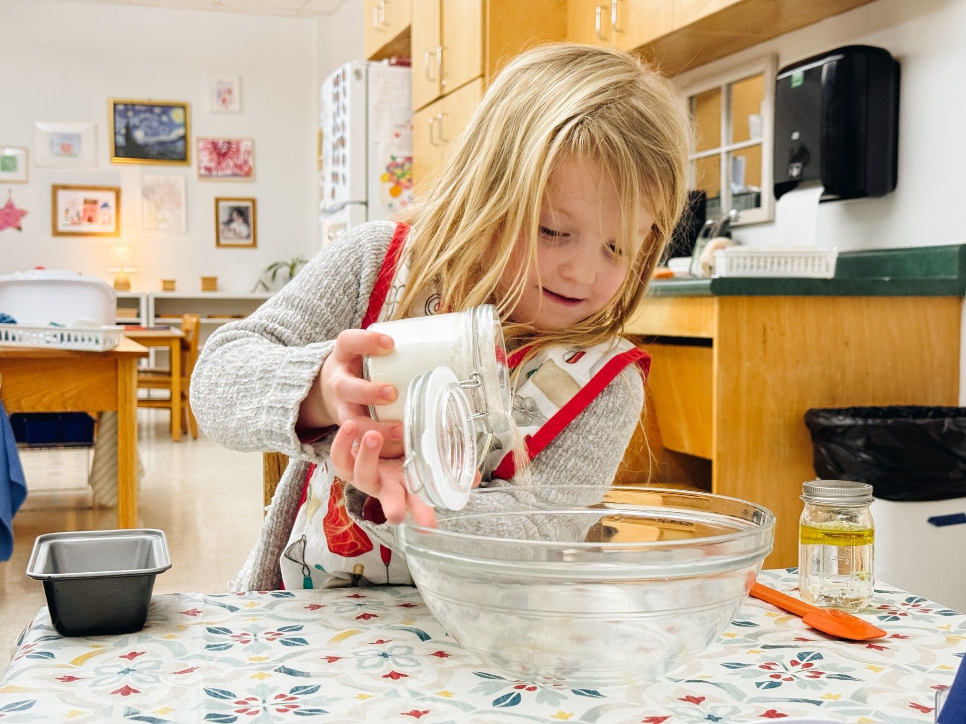 A primary child is adding dry ingredients to a bowl for bread making.