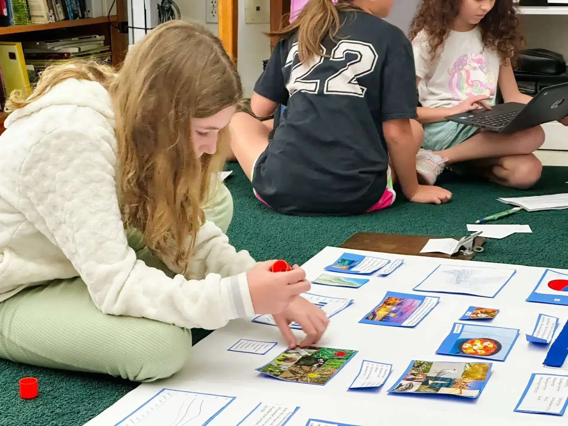 Girl gluing photos to a poster on the floor with two others nearby.