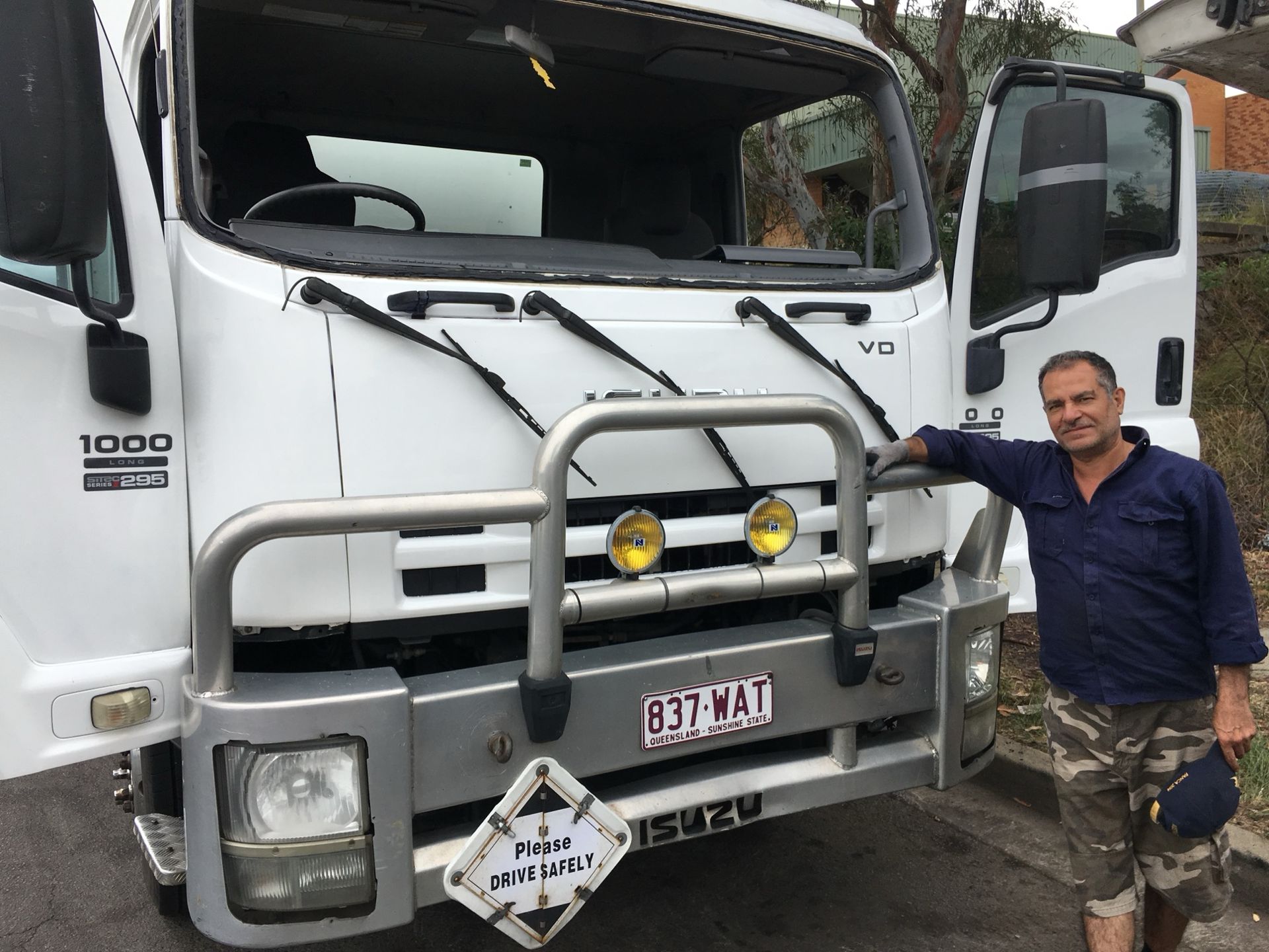 Man standing beside a white truck with front bull bar and headlights on in a parking lot