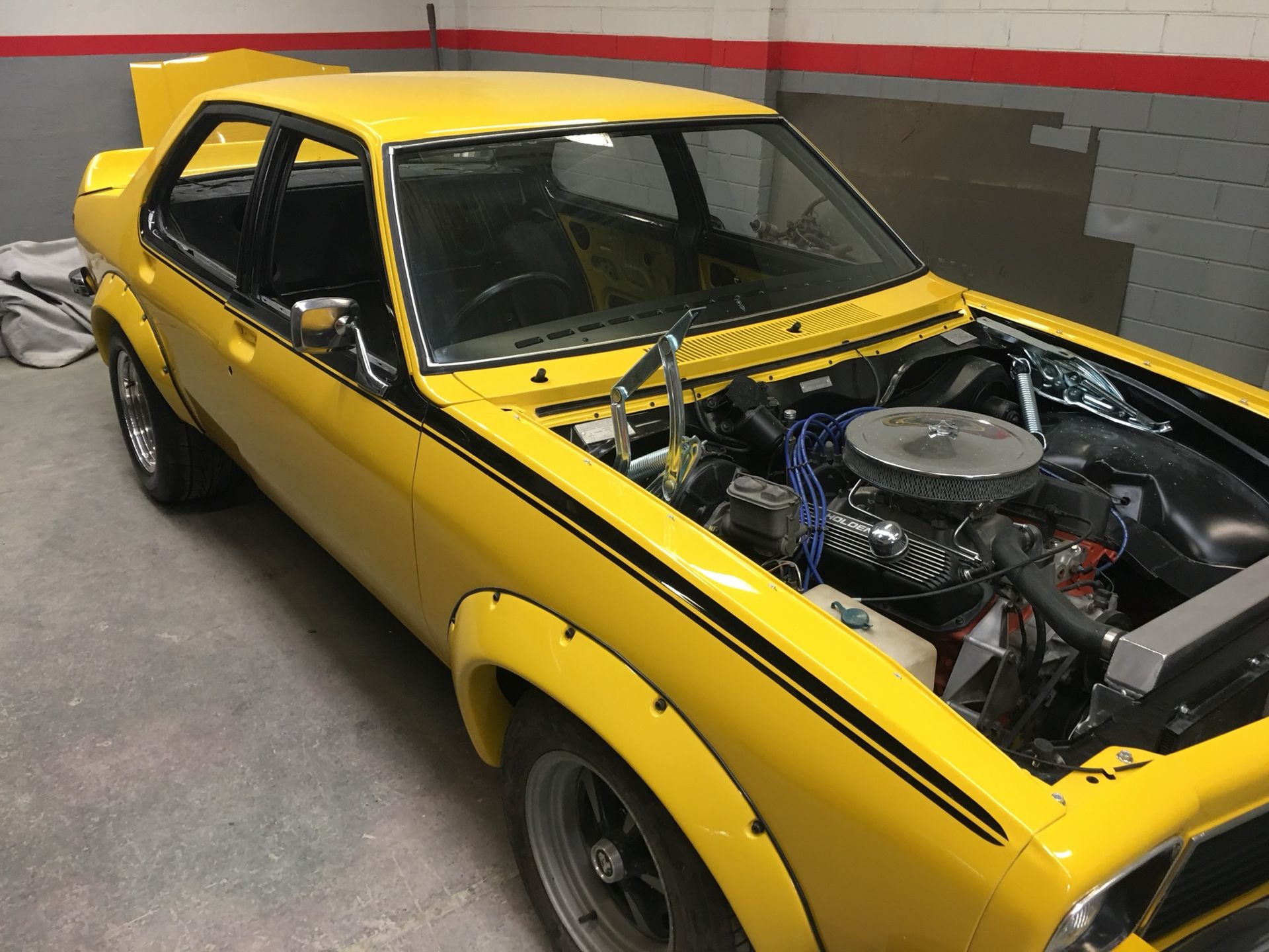 Yellow classic car with hood open, showing engine in a garage
