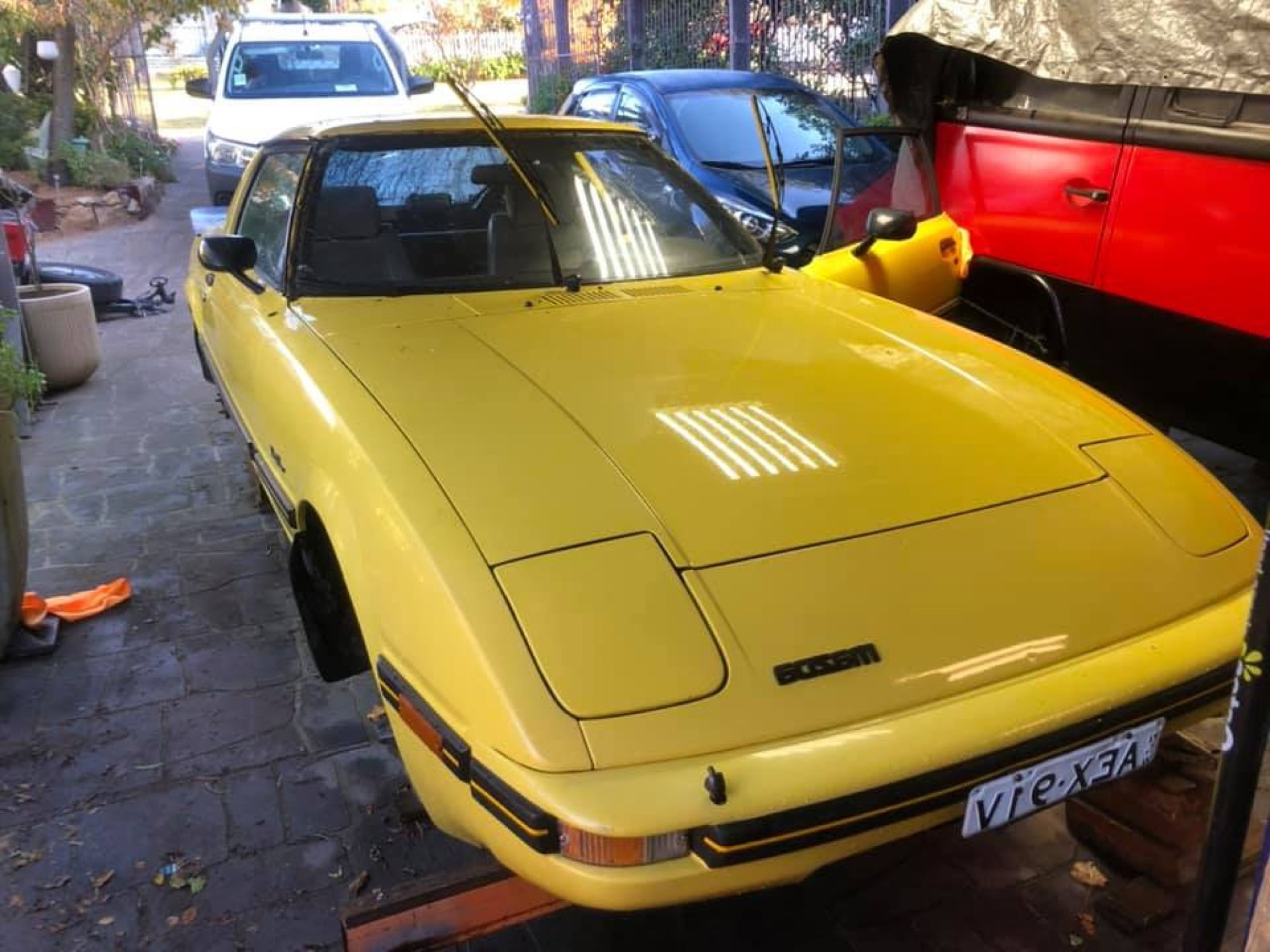 Yellow sports car parked outdoors beside a red vehicle in a driveway.