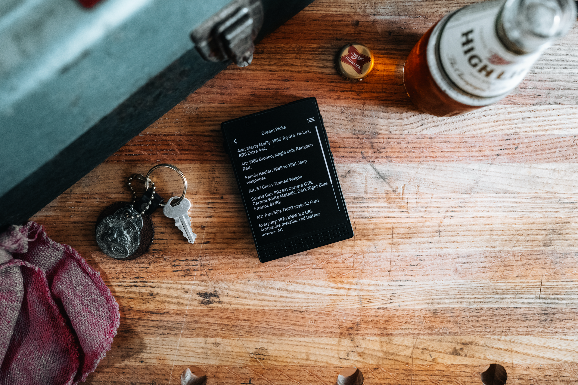Wooden table with beer bottle, keys, black phone, and a small box.