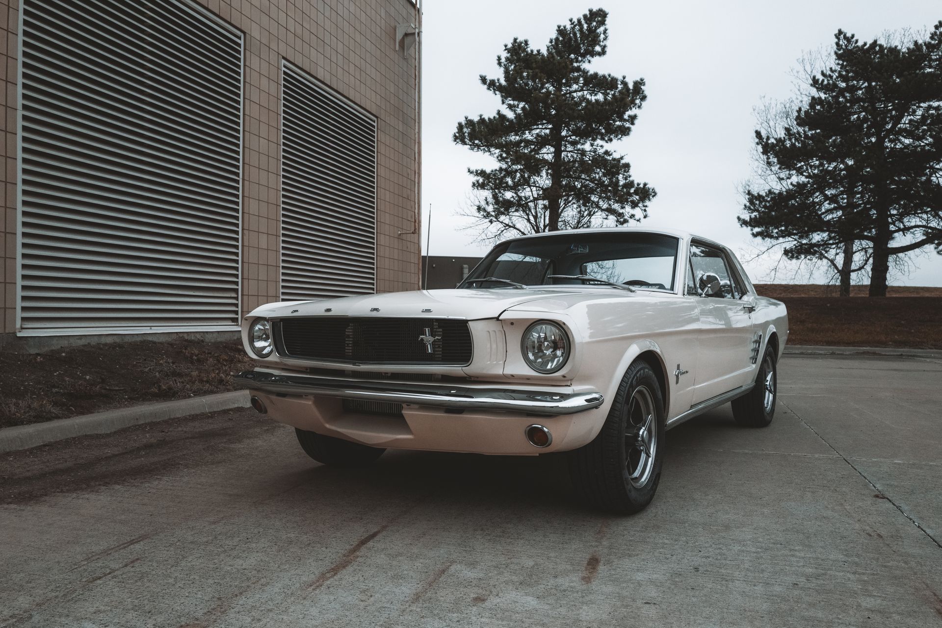 A white mustang is parked in front of a building.