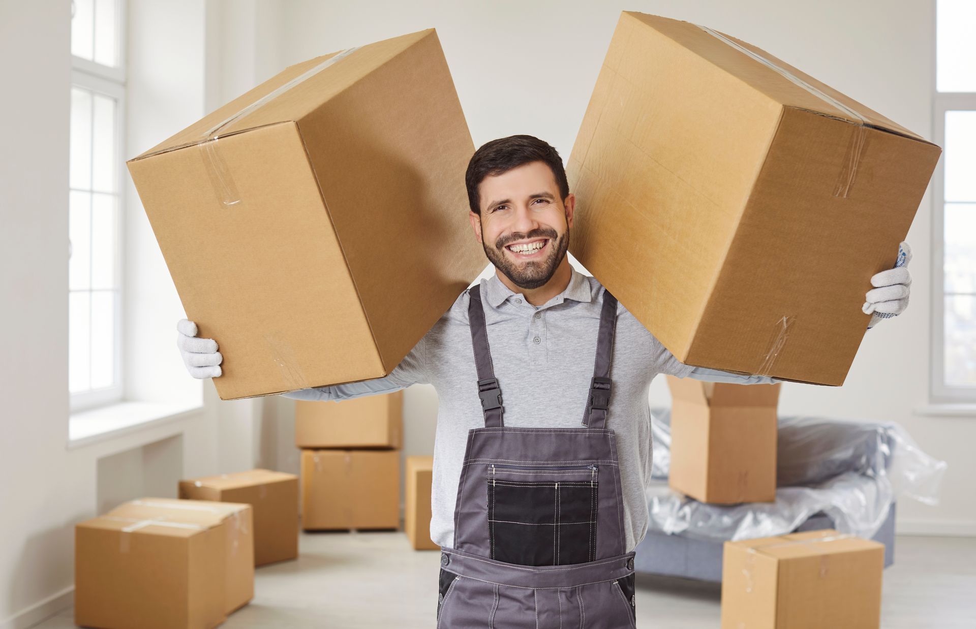 A mover holding two cardboard boxes inside a house filled with moving supplies