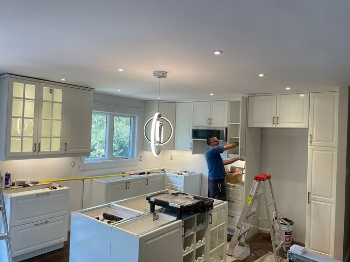 A man is working on a kitchen with white cabinets and a ladder.