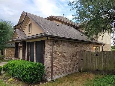 A brick house with a brown roof and a wooden fence in front of it.