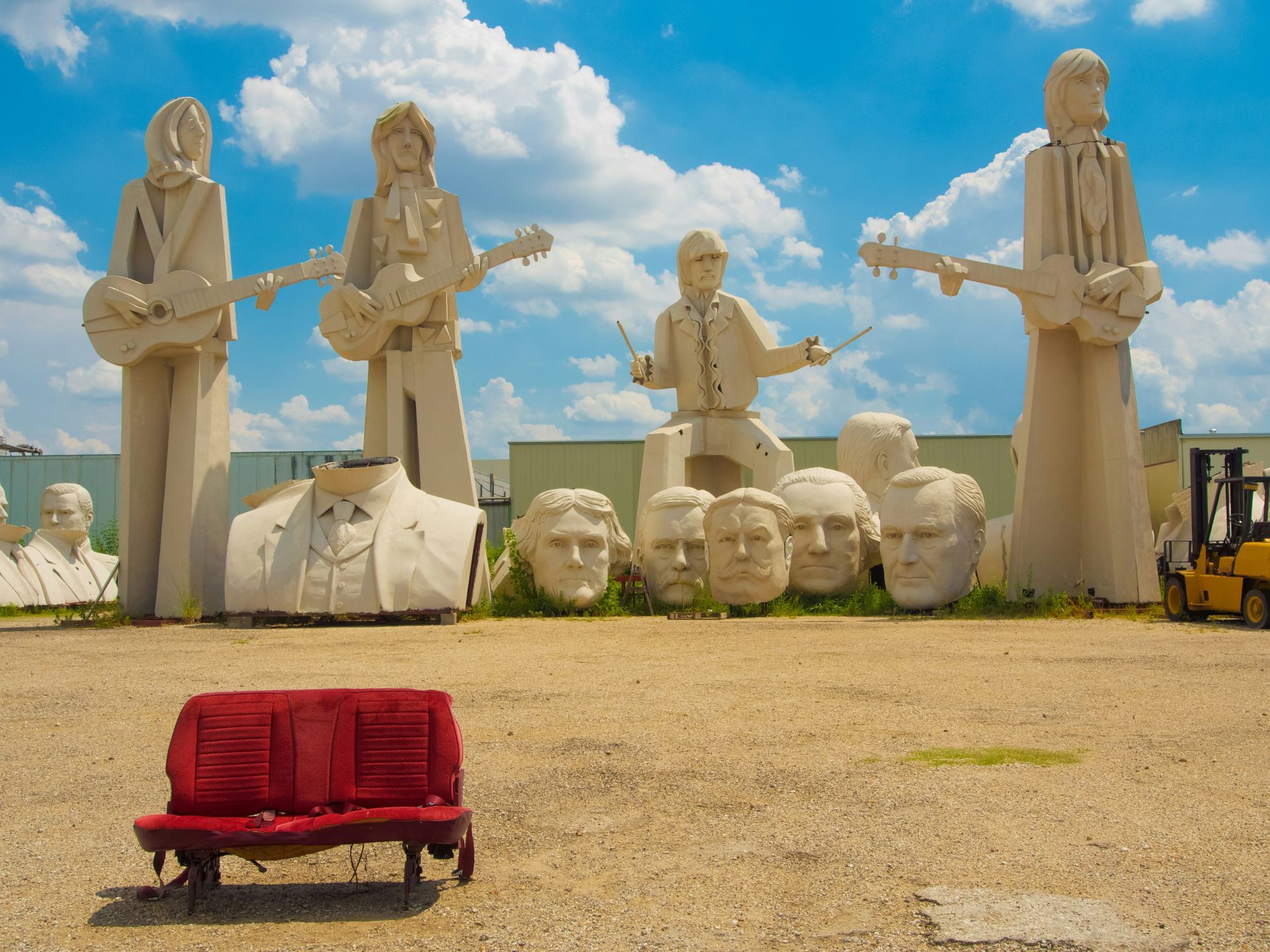 A red bench is sitting in front of a statue of a man playing a guitar.