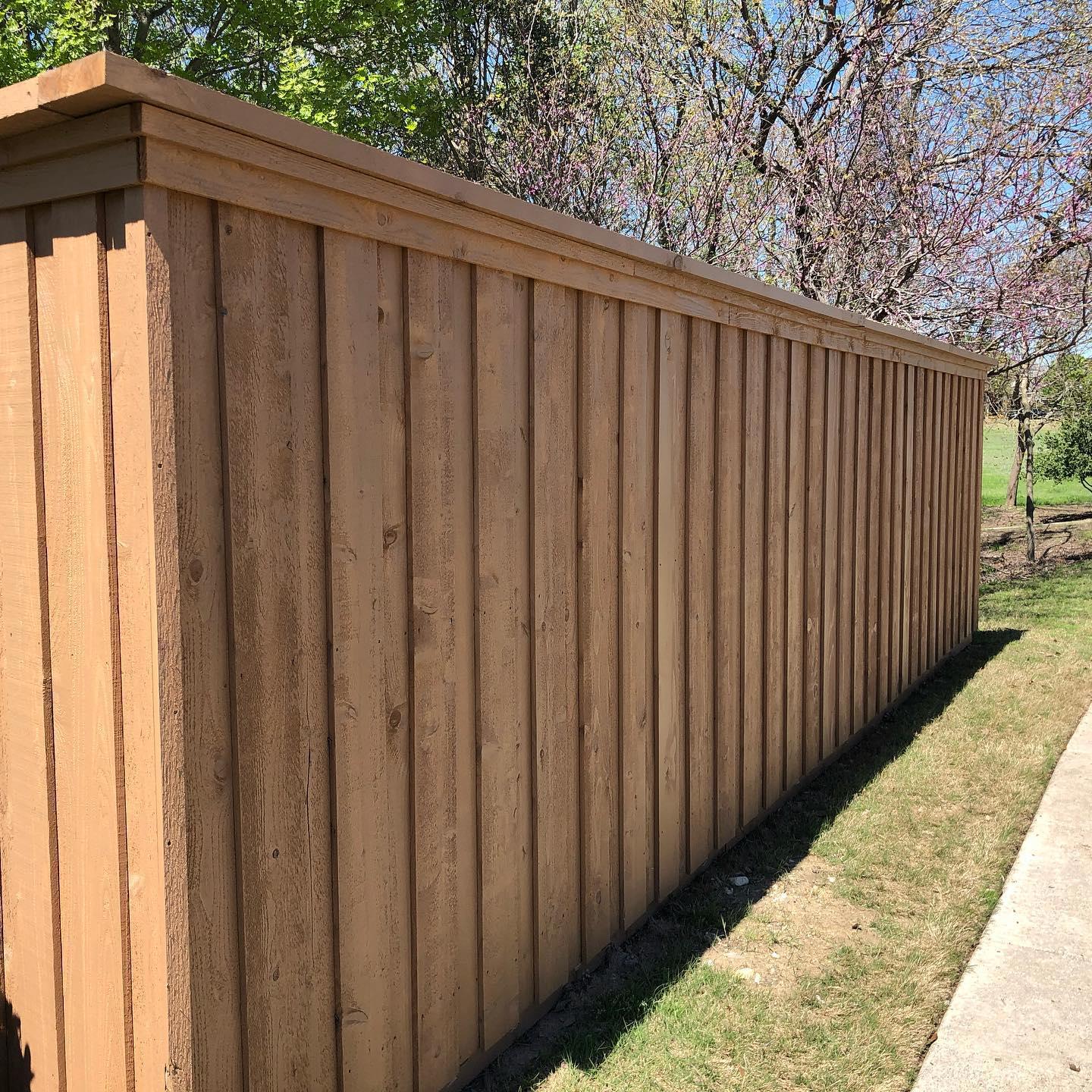 A wooden fence is sitting next to a sidewalk.