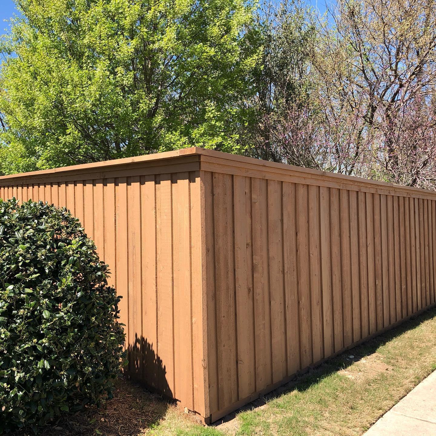 A wooden fence is sitting on the side of a sidewalk next to a bush.