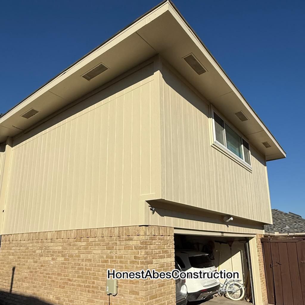 Tan two-story house with a brick base and garage. Blue sky in the background. 