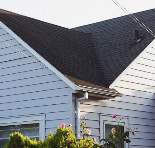 Blue house with dark roof and white trim; windows and greenery in foreground.