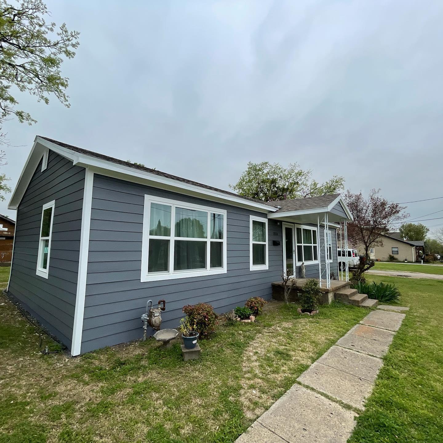 A small gray house with white trim and windows is sitting on top of a lush green lawn.