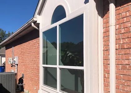 Brick house exterior with a large window and arched top, white trim, and a blue sky.