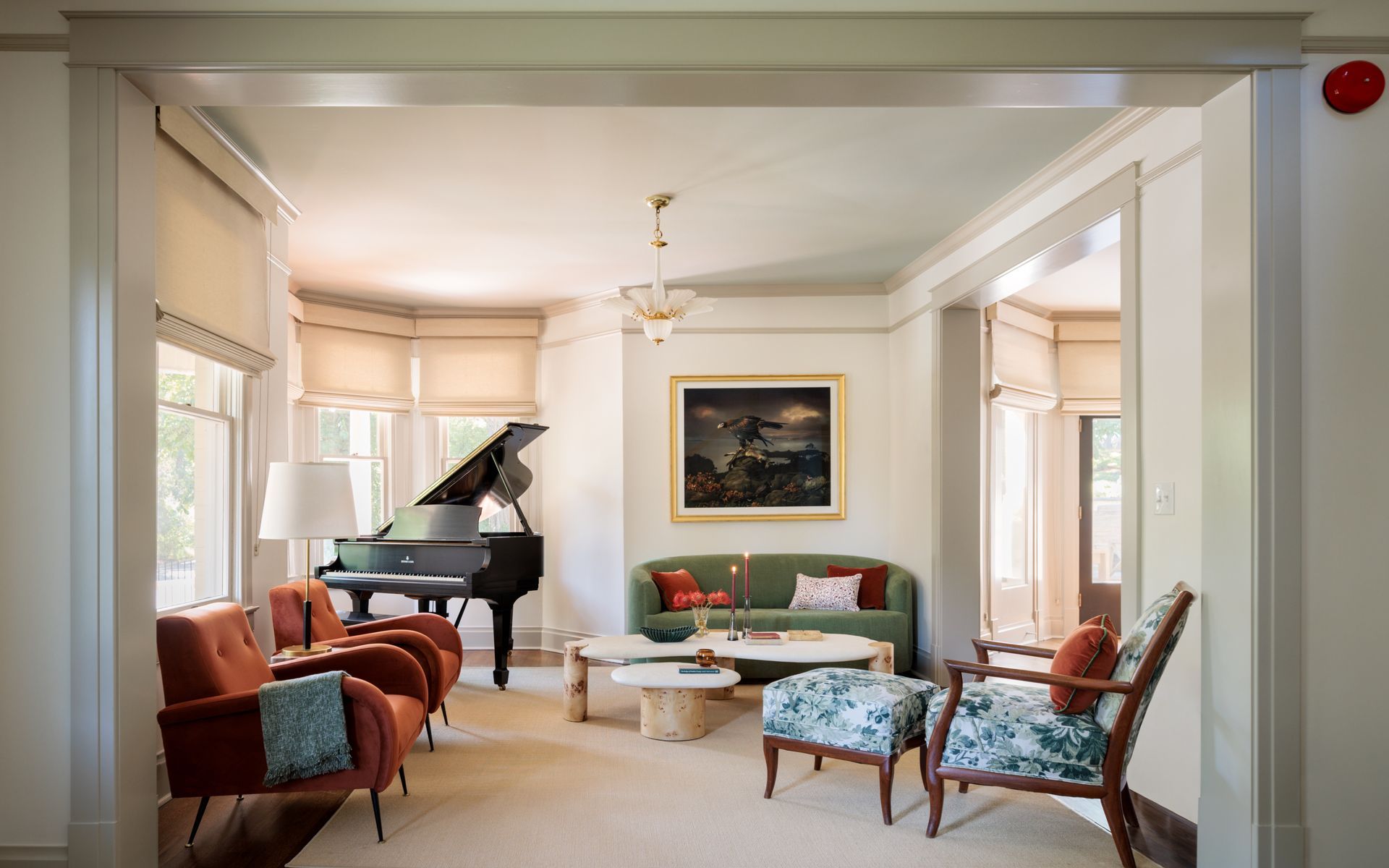 A living room with a piano and a couch and roman shades over bay windows