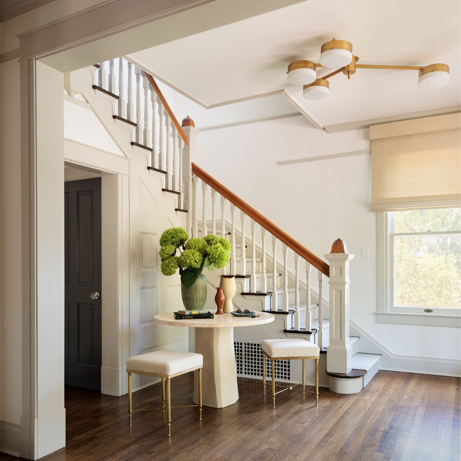 A staircase with a table and chairs in front of it and roman shades in the entry way