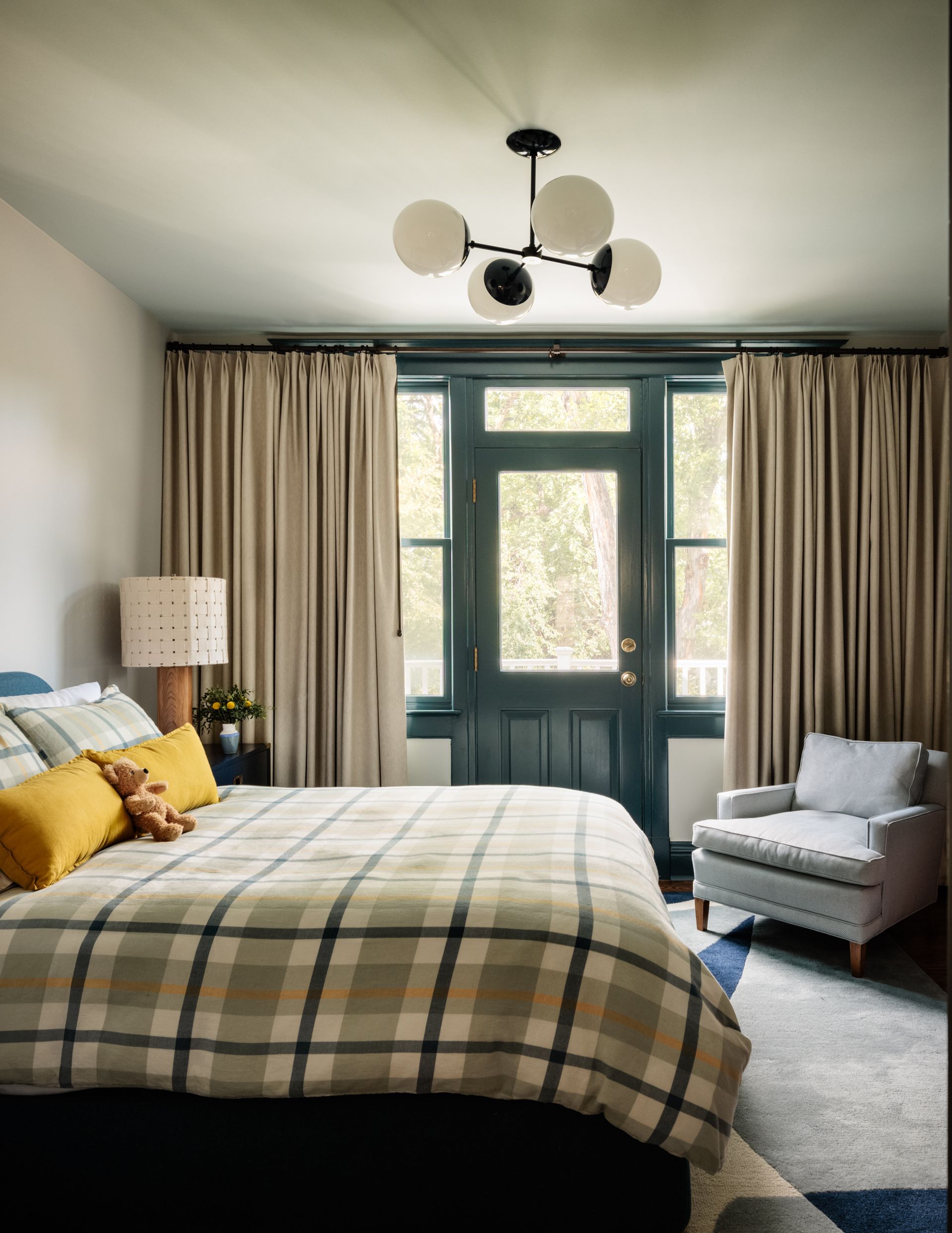 A bedroom with a bed , chair , lamp and door and tan drapes over french doors