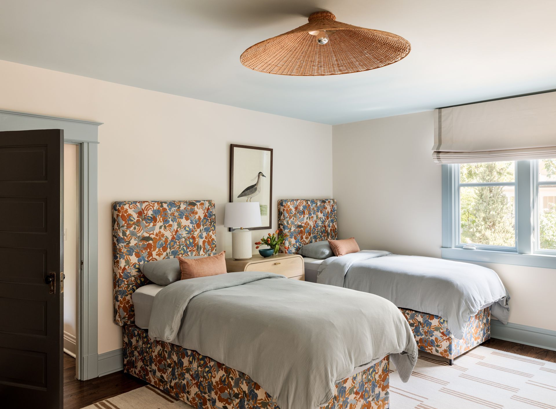 A bedroom with two twin beds and a ceiling fan and custom roman shades over the windows