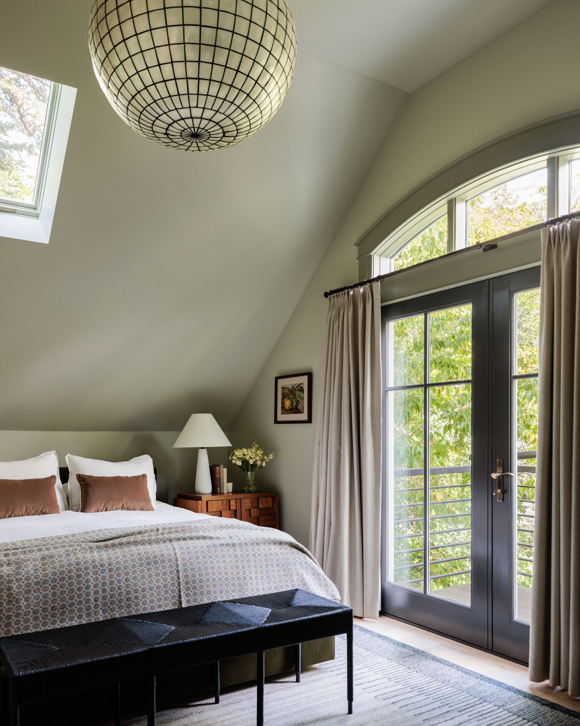 A bedroom with a large bed and a large window and tan drapes over french doors