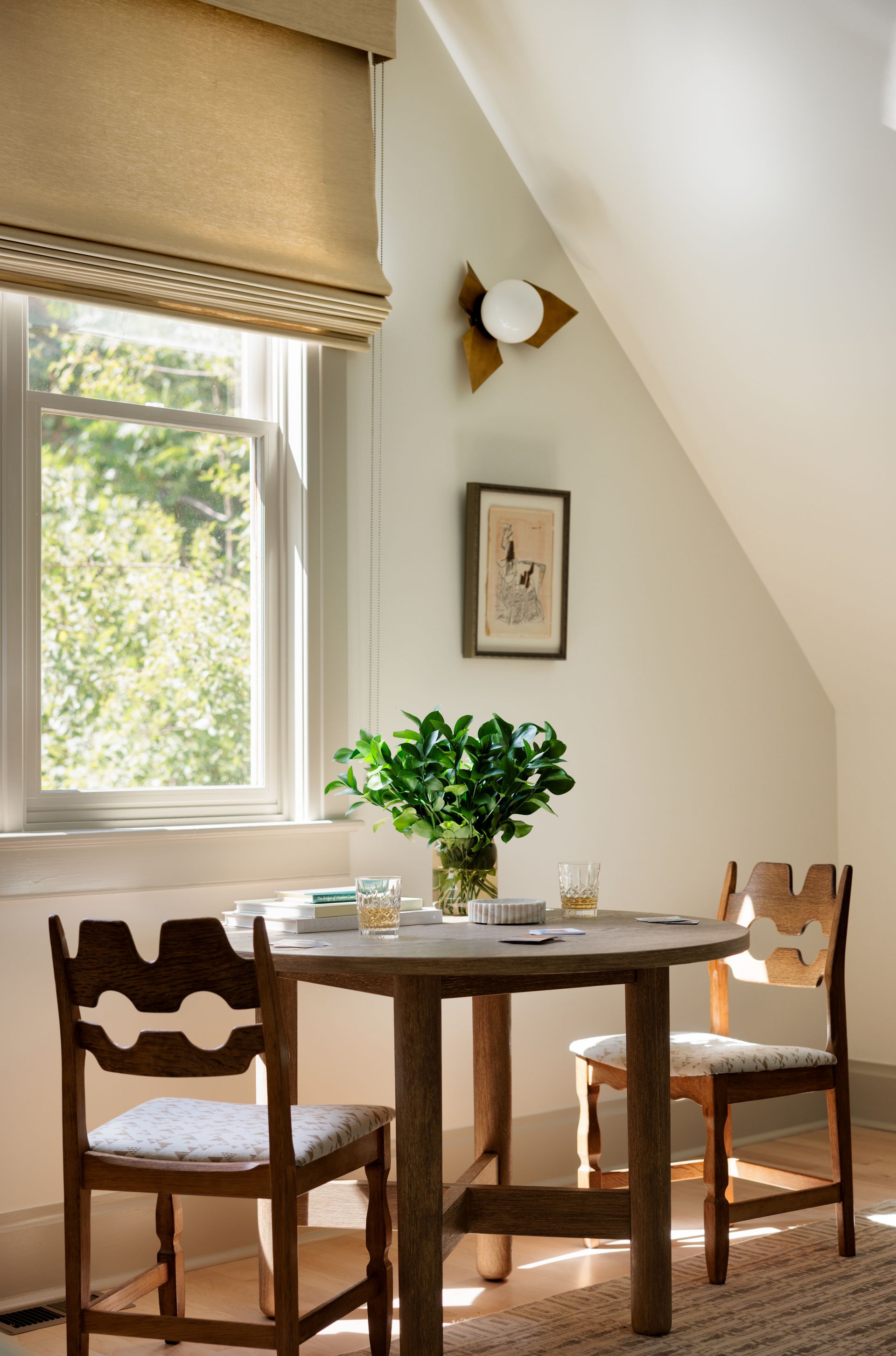 A table and chairs in a room with a window with roman shades