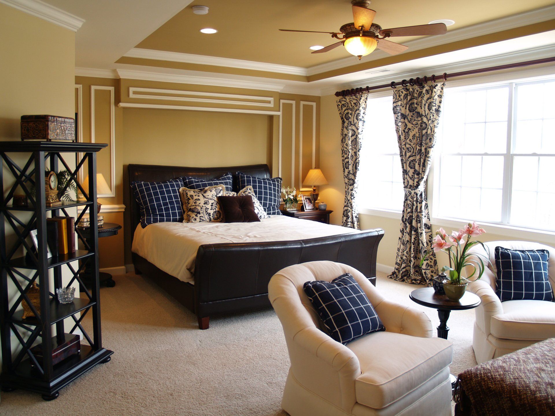 A bedroom with a large bed and a ceiling fan and large windows with custom drapes