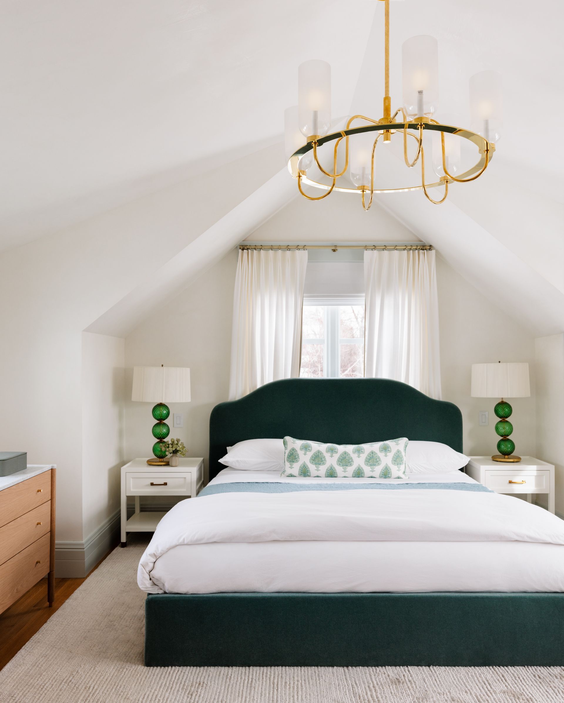 A bedroom with a bed and a chandelier hanging from the ceiling and drapes behind the bed