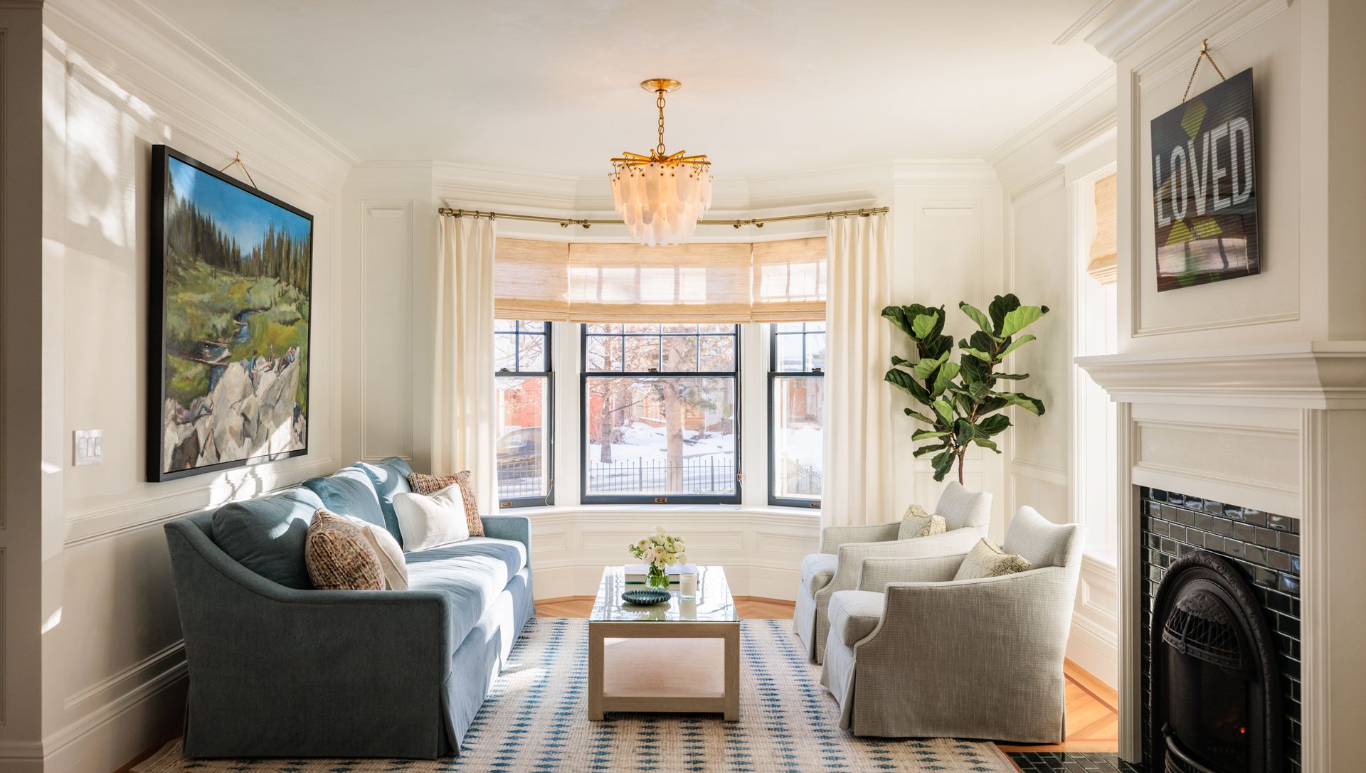 A living room with a couch , chairs , coffee table and fireplace with a bay window with drapes
