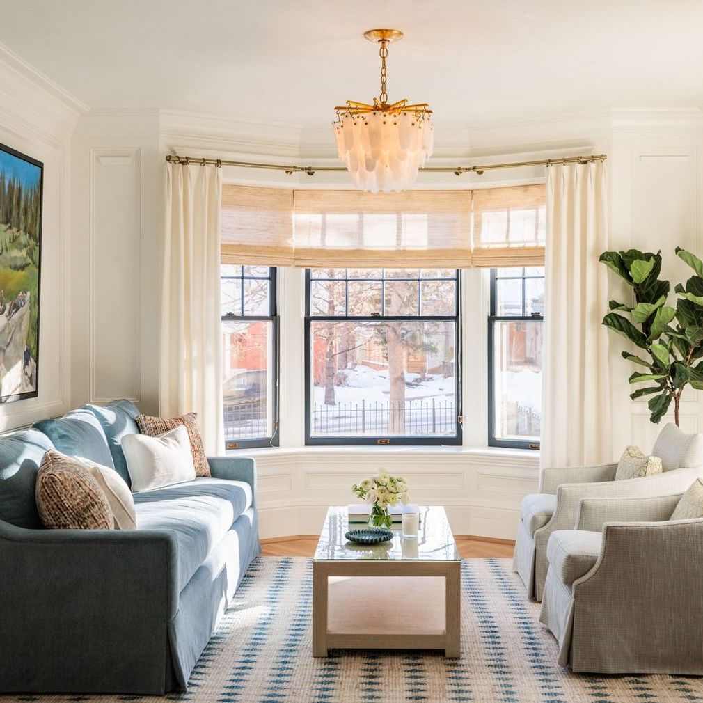 A living room filled with furniture and a bay window with woven wood shades and cream drapes