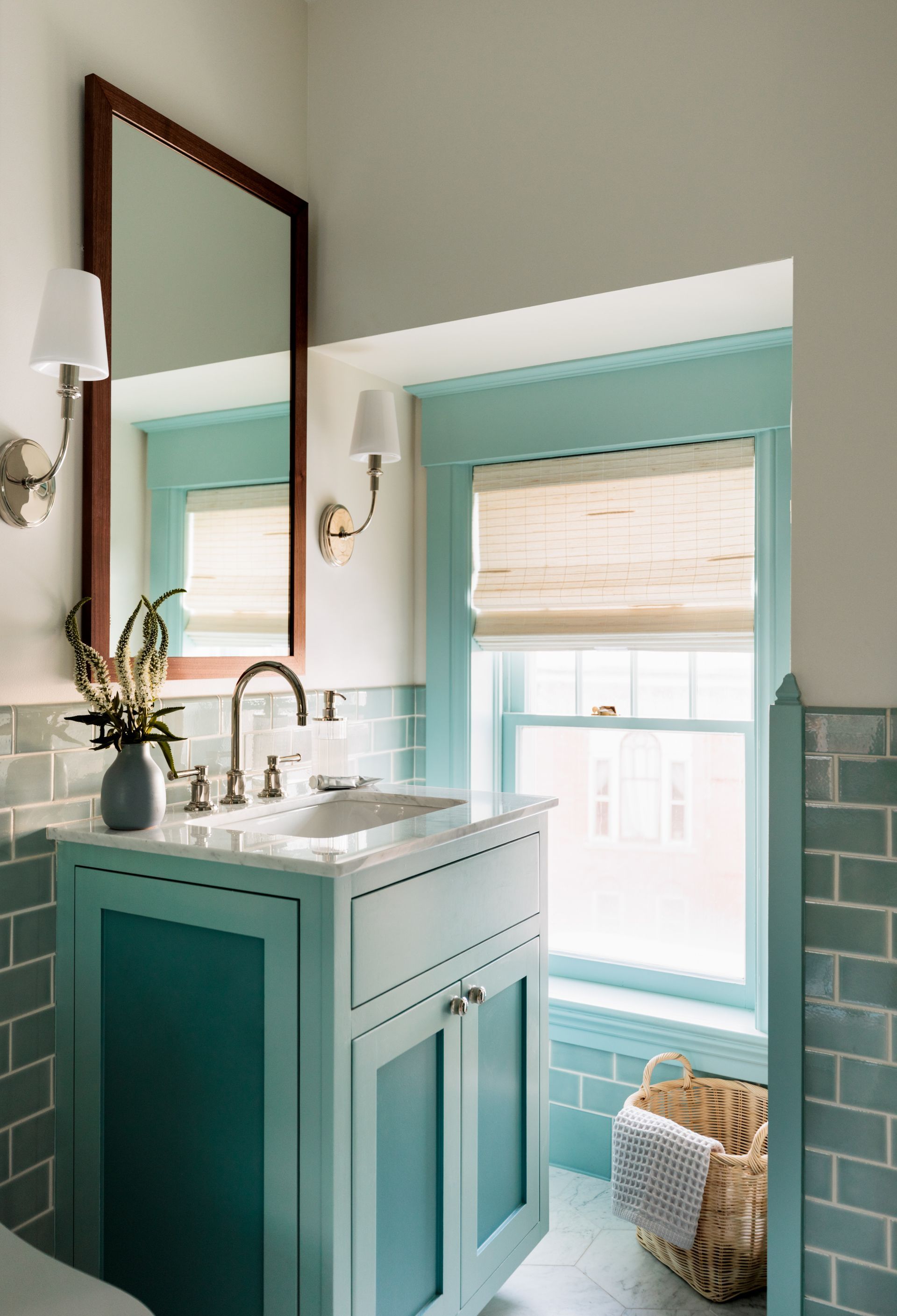 A bathroom with a sink , mirror , toilet and window and woven wood blinds
