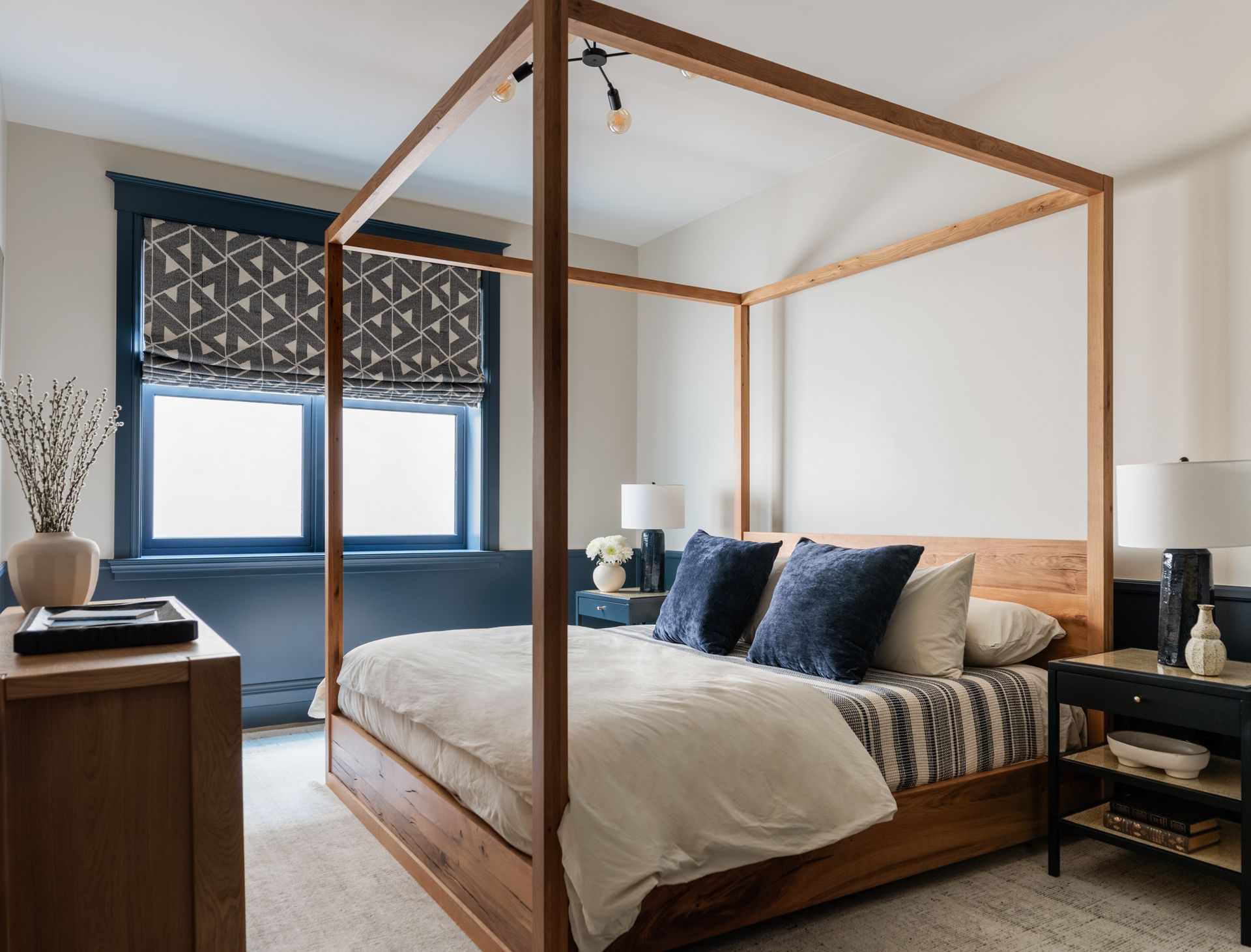 A bedroom with a canopy bed and a window and navy blue printed roman shades