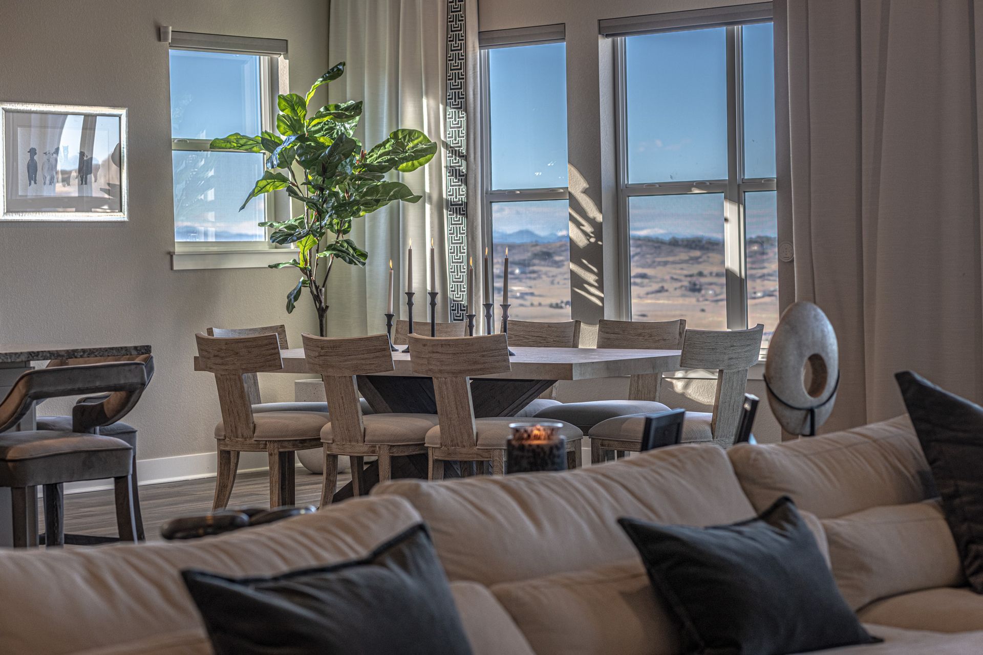 A living room with tall windows, a couch , table and chairs and a view of the desert.