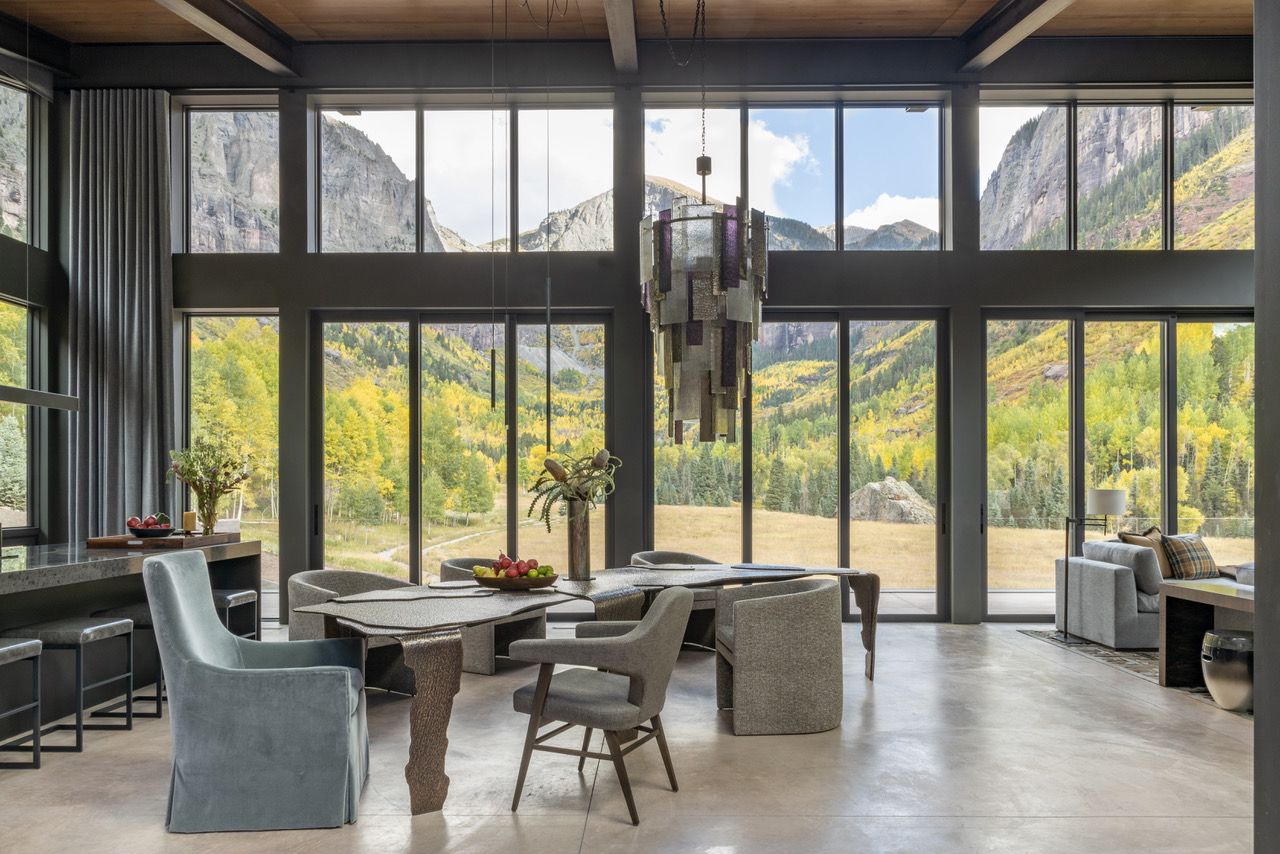 A living room with a lot of windows and mountains in the background.