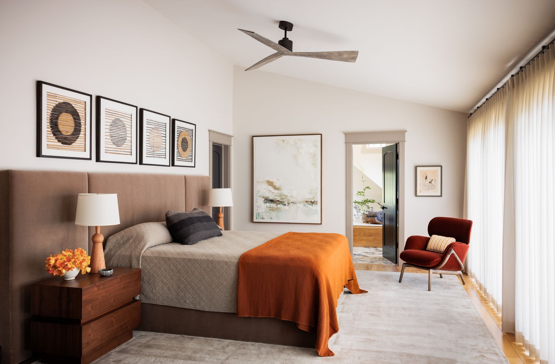 A bedroom with a bed and a ceiling fan and white drapes over sliding doors