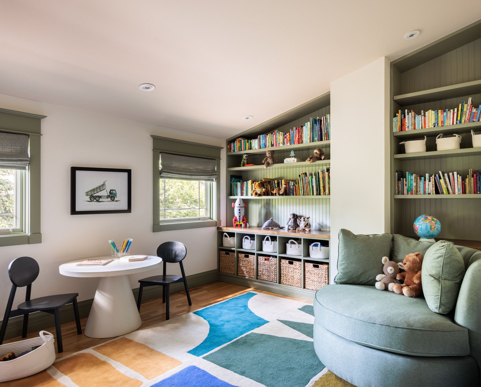 A living room with a couch , table , chairs and shelves filled with books along with blackout roman shades