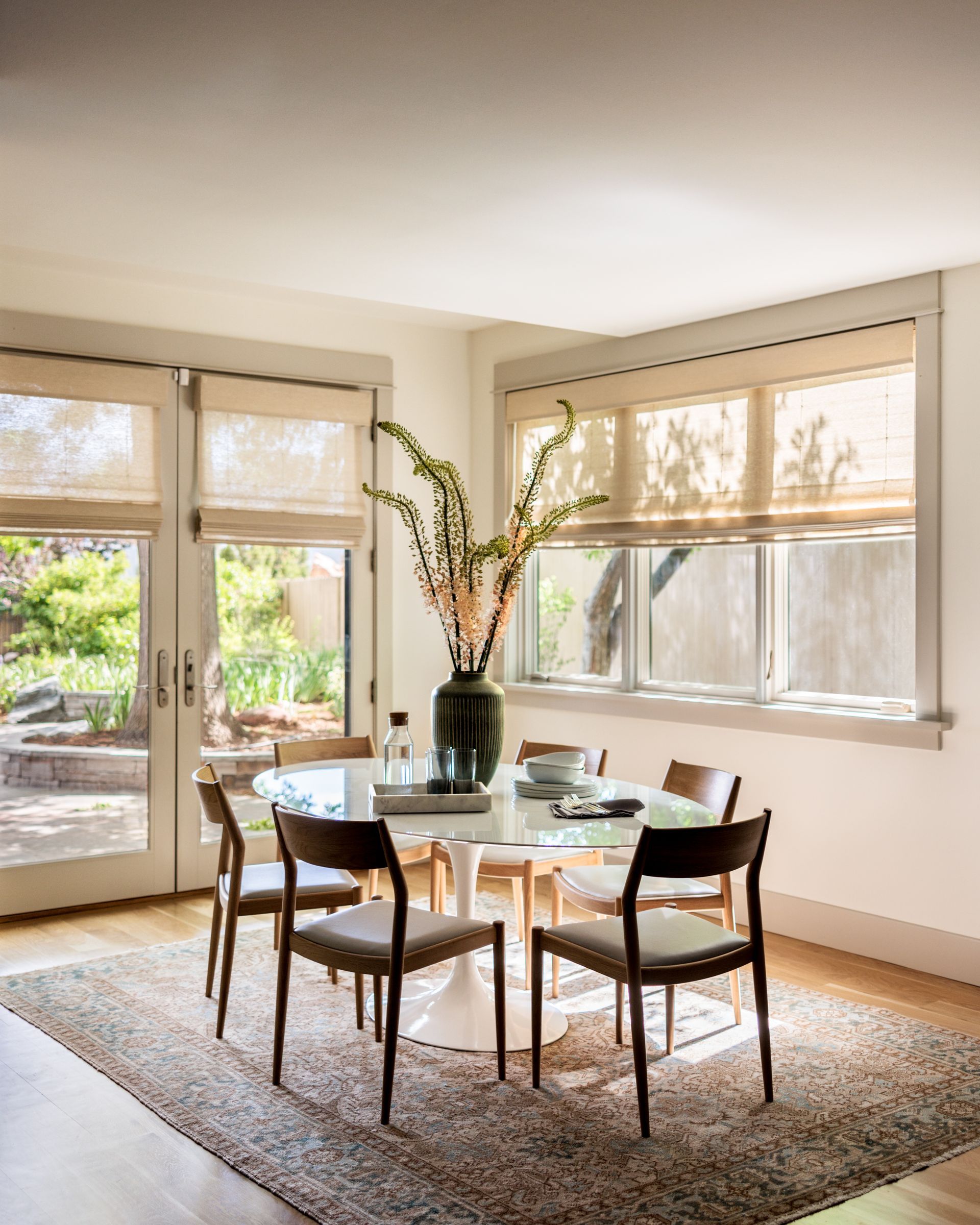 A dining room with a table and chairs and a vase of flowers on the table and transparent motorized shades