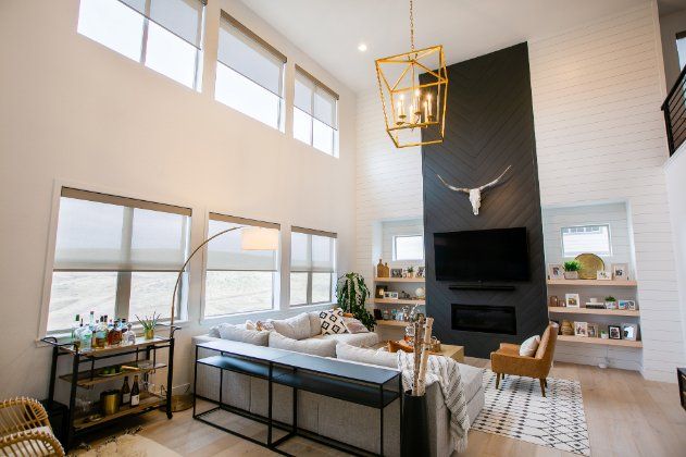 A living room with modern windows, roller shades, couch , chairs , television and fireplace.