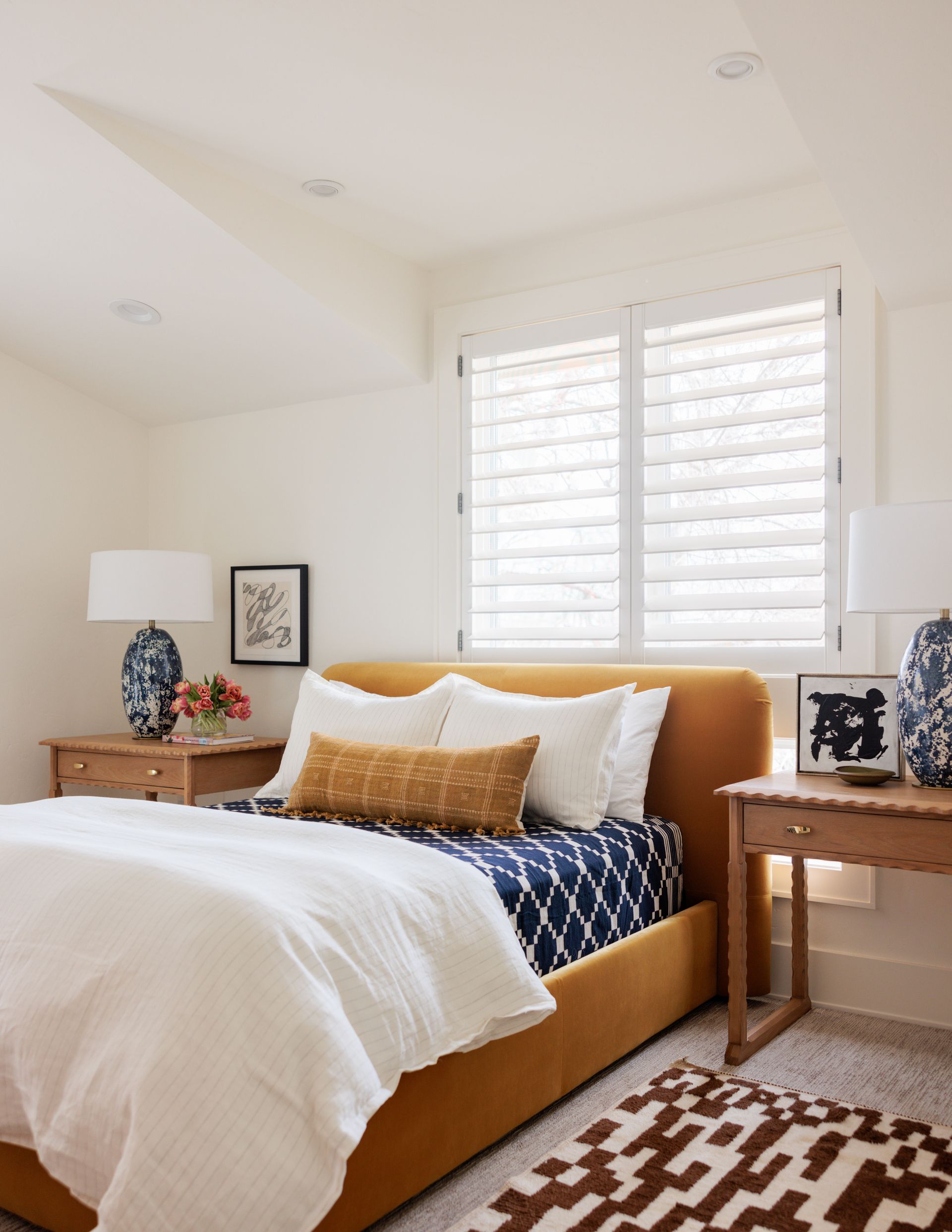 A bedroom with a yellow bed and white sheets with window behind the bed