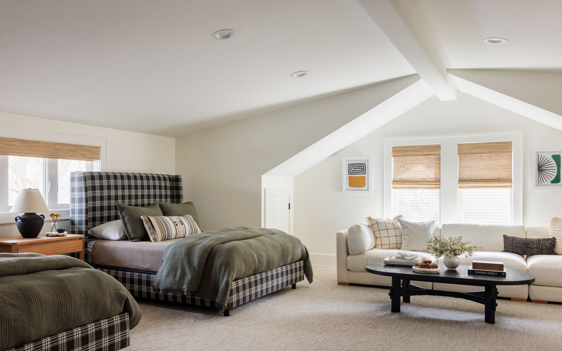 A bedroom with two beds , a couch , and a coffee table and woven wood shades in a gable window