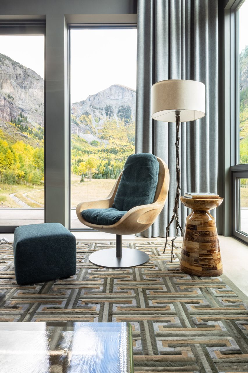 A living room with tall windows, custom motorized drapes, a chair , lamp , ottoman and a large window.