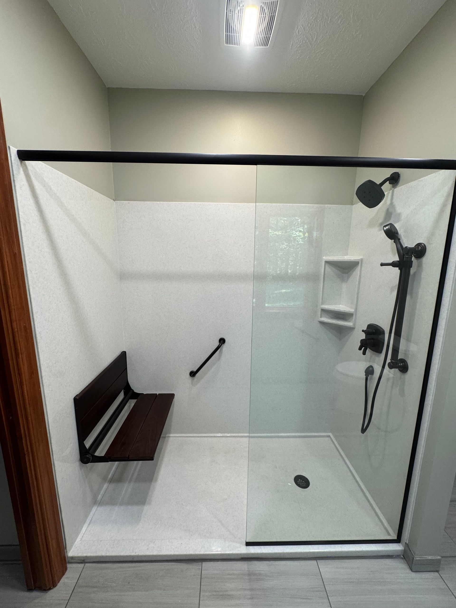 Accessible shower with glass doors, built-in seat, grab bar, and dark fixtures against white walls.