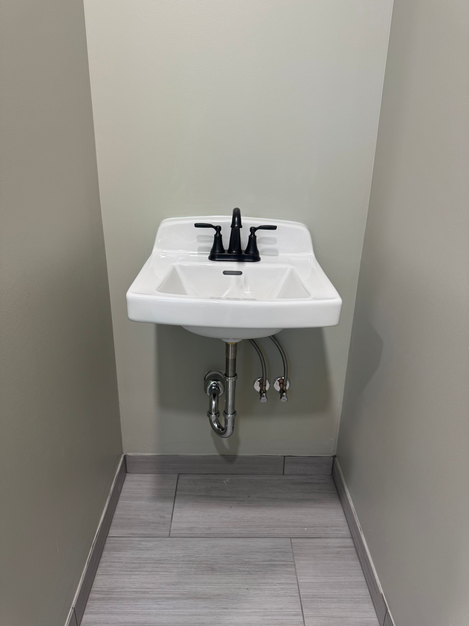 White wall-mounted sink with black faucet in a small, tiled space.