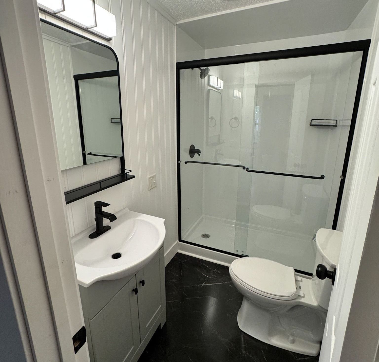 A bathroom with a toilet , sink , mirror and shower.
