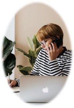 A woman is sitting in front of a laptop computer talking on a cell phone.