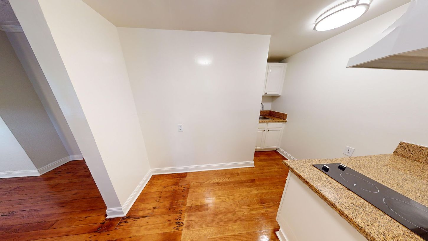 Interior view of a kitchen with light-colored cabinets and countertops, wood flooring, and white walls.