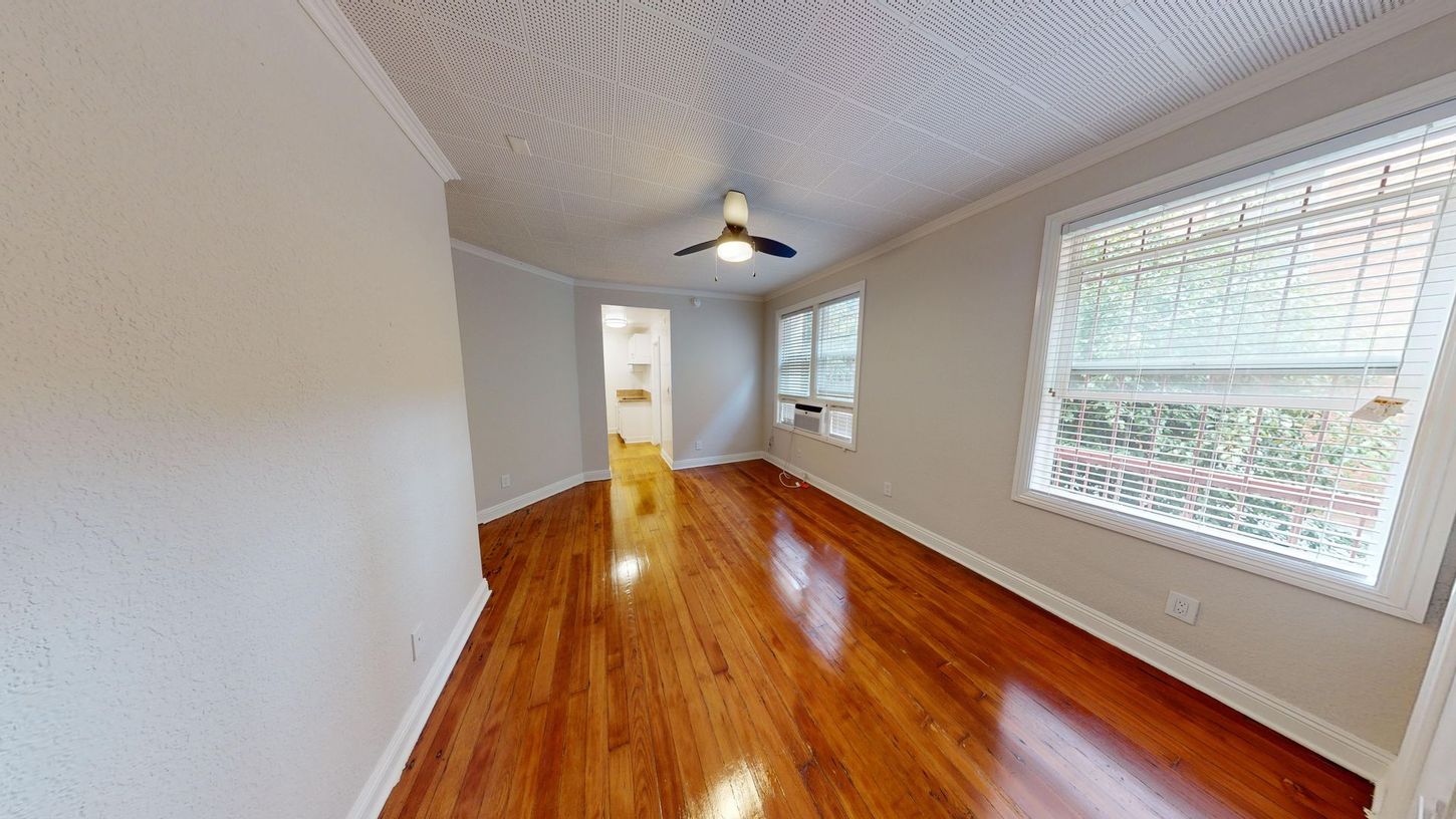 Empty room with wood floors, patterned ceiling, and windows with white frames.
