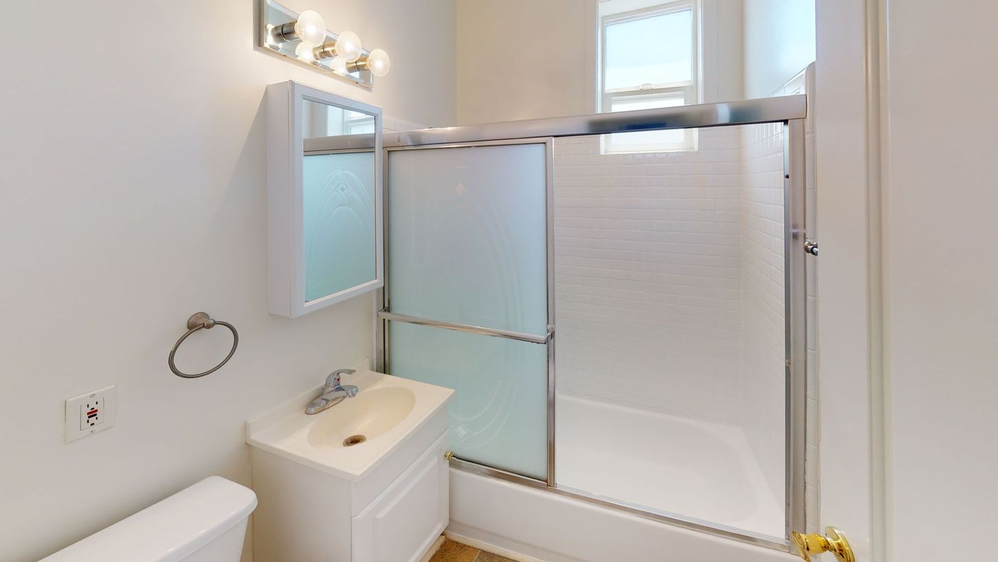 Bathroom with white walls, shower, vanity, toilet, and a window.