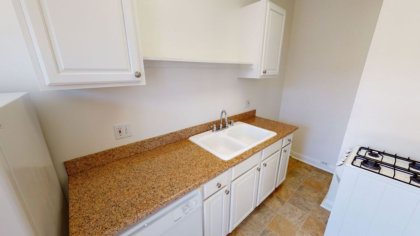 Kitchen with white cabinets, speckled countertop, sink, and gas stove.